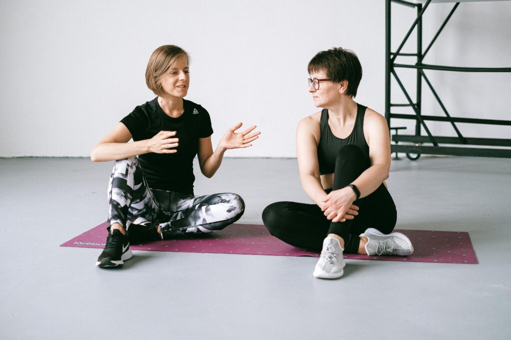 Two women talking while sitting on yoga mats, focusing on fitness and health.